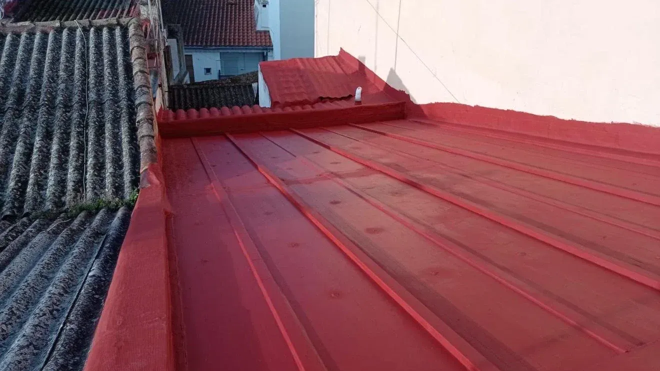 Cubierta metálica recién impermeabilizada con pintura roja, rematada contra la pared y junto a un tejado de placas viejas